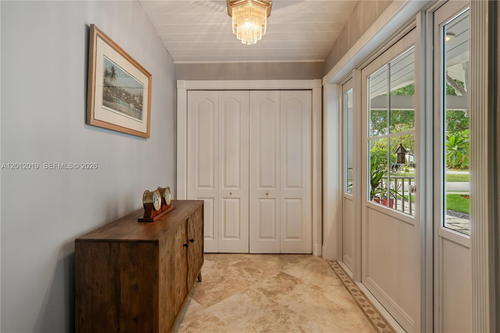 An entryway features a wood console table, a crystal chandelier, and a white closet — 13401 SW 74th Ave, Pinecrest FL 33156, PINECREST, FL