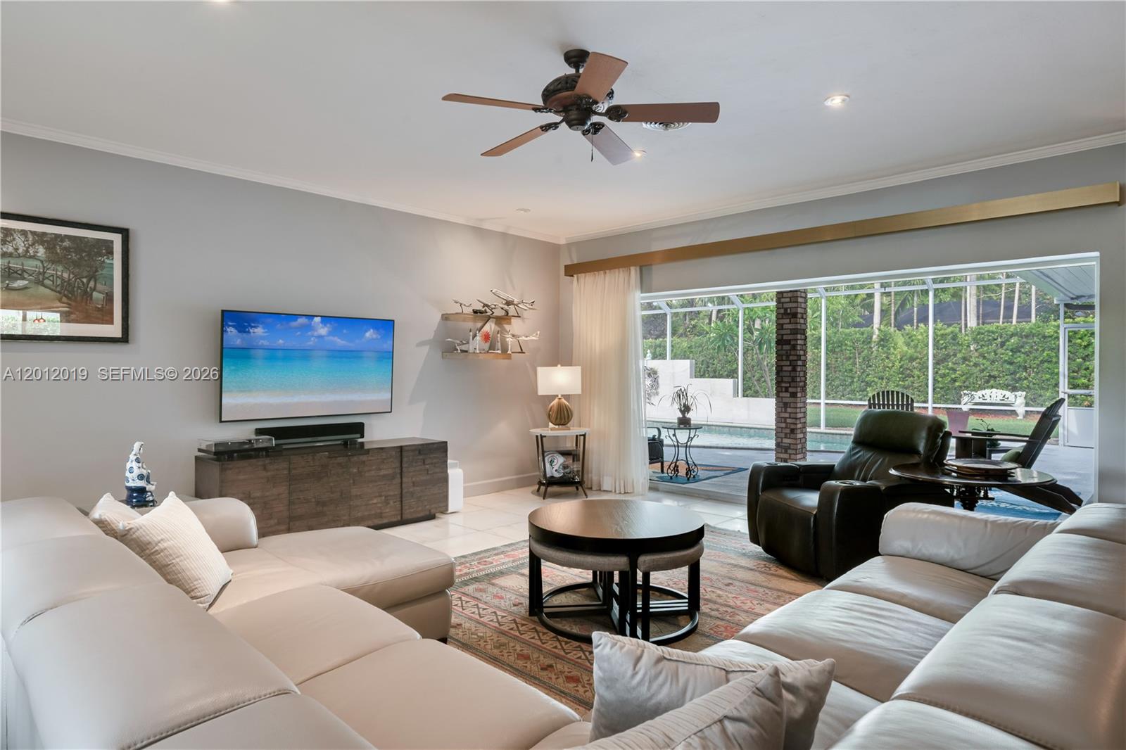 A living room features a sectional sofa, television, and large sliding doors opening to a pool — 13401 SW 74th Ave, Pinecrest FL 33156, PINECREST, FL