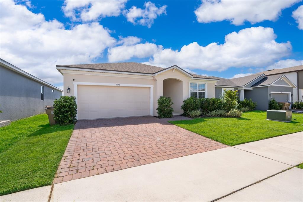 A single-story house with a beige stucco exterior, a brick paver driveway, and a garage — 1073 TURQUOISE WAVES COVE, KISSIMMEE, FL