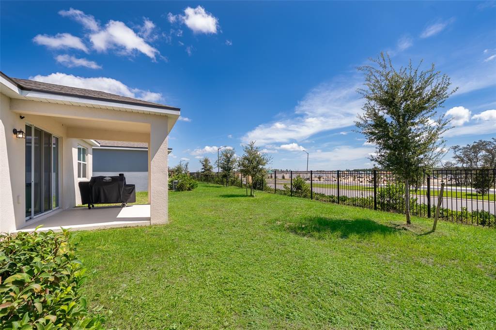 A backyard with a covered patio, a grill, and a black metal fence under blue skies — 1073 TURQUOISE WAVES COVE, KISSIMMEE, FL