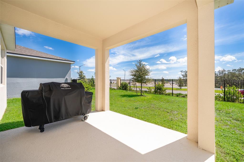 A covered concrete patio features a grill under a black cover and a fenced backyard — 1073 TURQUOISE WAVES COVE, KISSIMMEE, FL