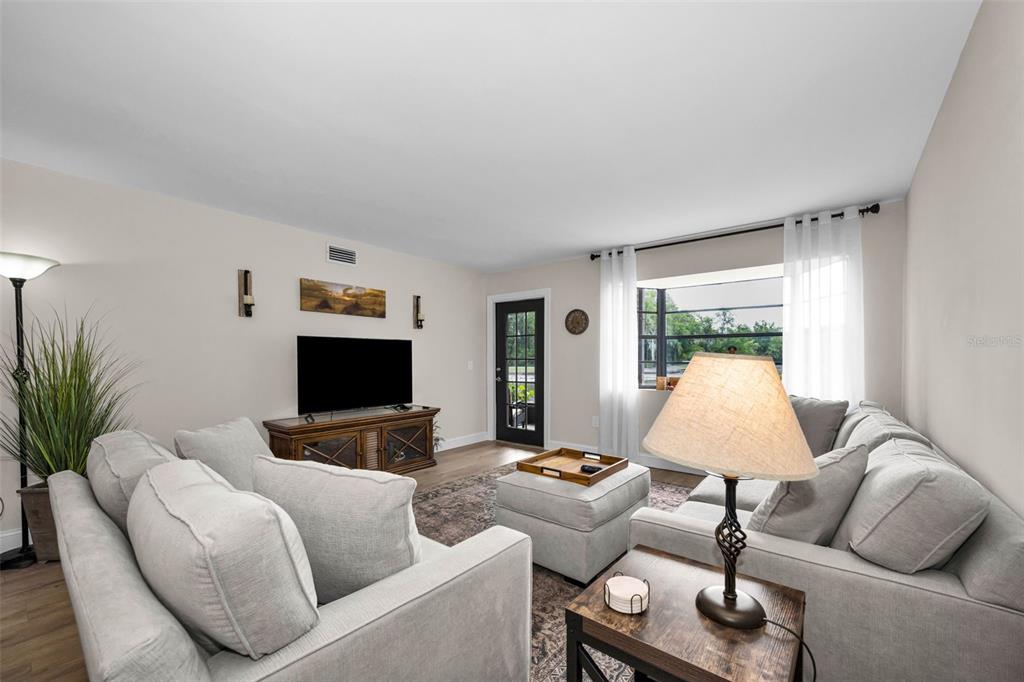 A living room features light gray sofas, a television on a wooden stand, and flooring — 12025 PROCTOR LOOP UNIT 3, NEW PORT RICHEY, FL