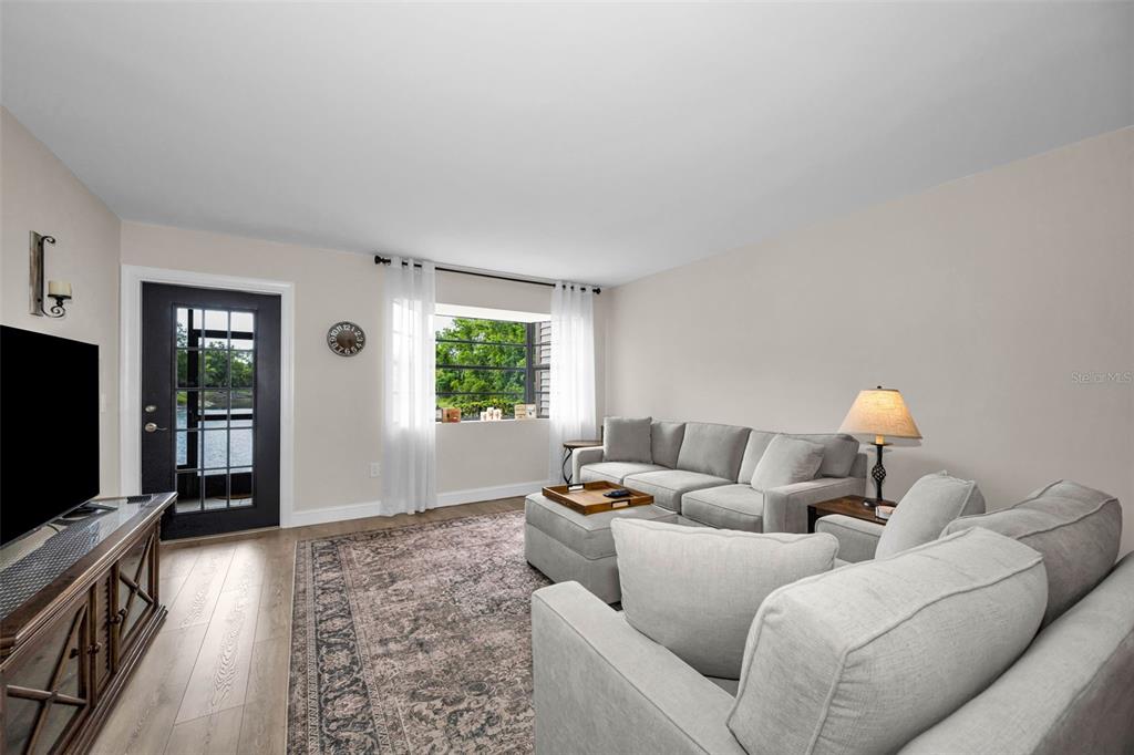 A living room features a grey sectional sofa, a patterned area rug, and a glass door — 12025 PROCTOR LOOP UNIT 3, NEW PORT RICHEY, FL