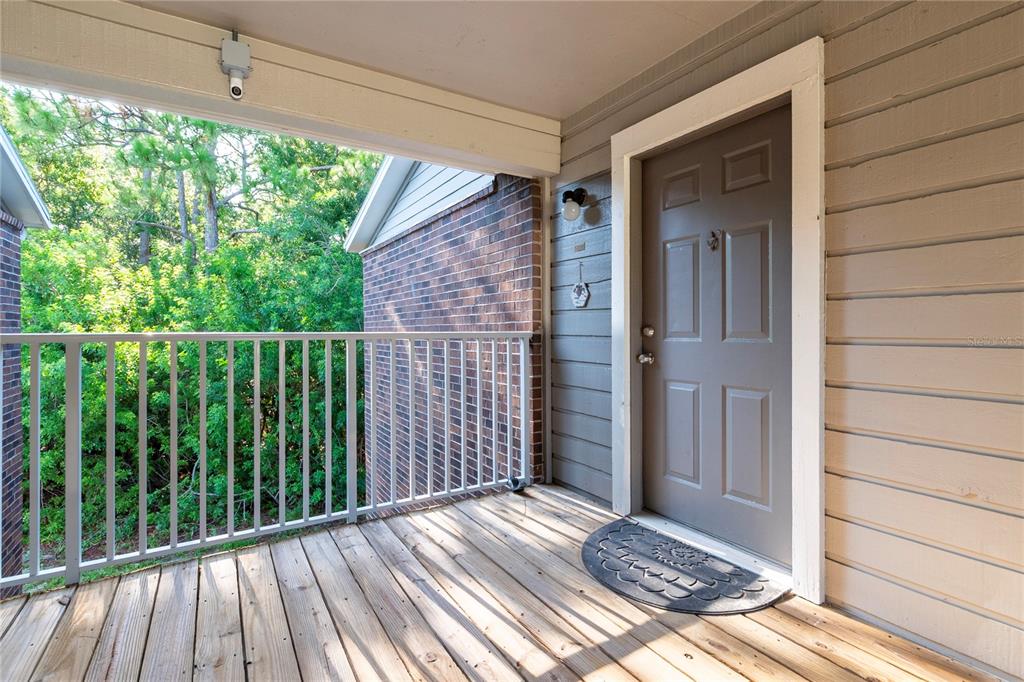 A wooden balcony features a gray front door, white railings, and a view of trees — 1400 GANDY BOULEVARD N UNIT 1708, ST PETERSBURG, FL