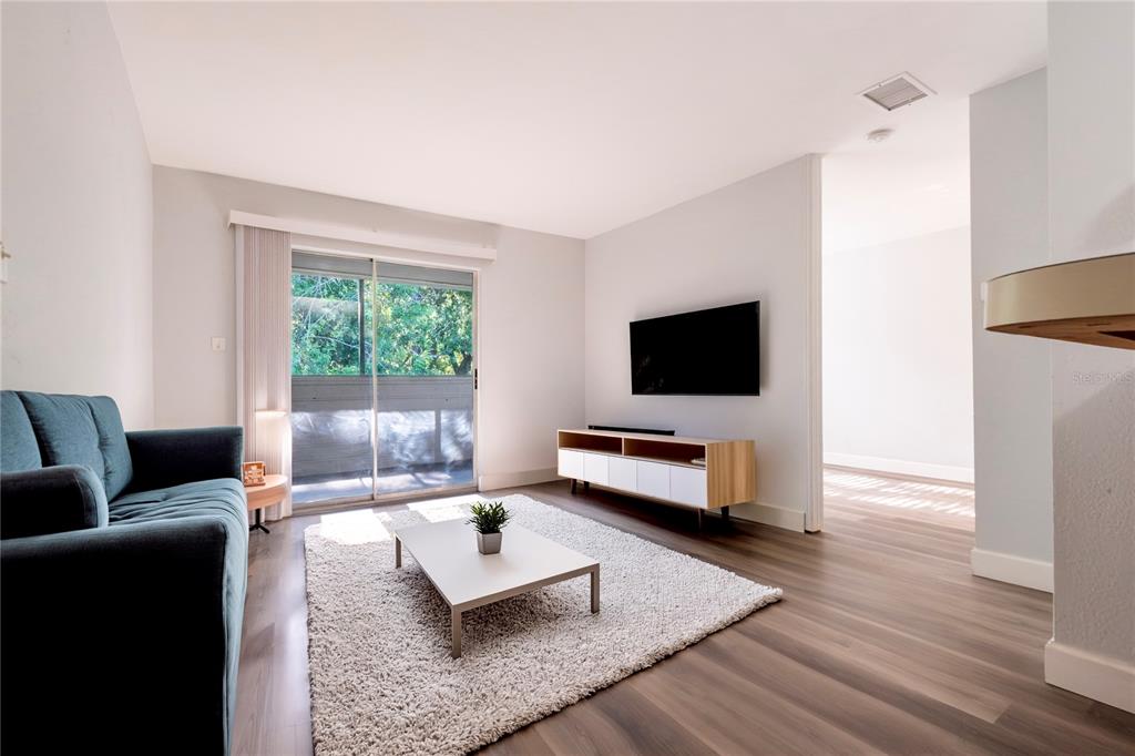A living room features a blue sofa, white coffee table, media console, and sliding glass doors — 1400 GANDY BOULEVARD N UNIT 1708, ST PETERSBURG, FL
