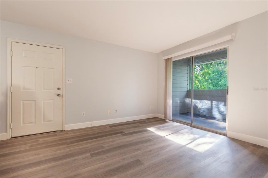 An empty room features light-colored walls, wood-look flooring, a white entry door, and sliding glass doors — 1400 GANDY BOULEVARD N UNIT 1708, ST PETERSBURG, FL