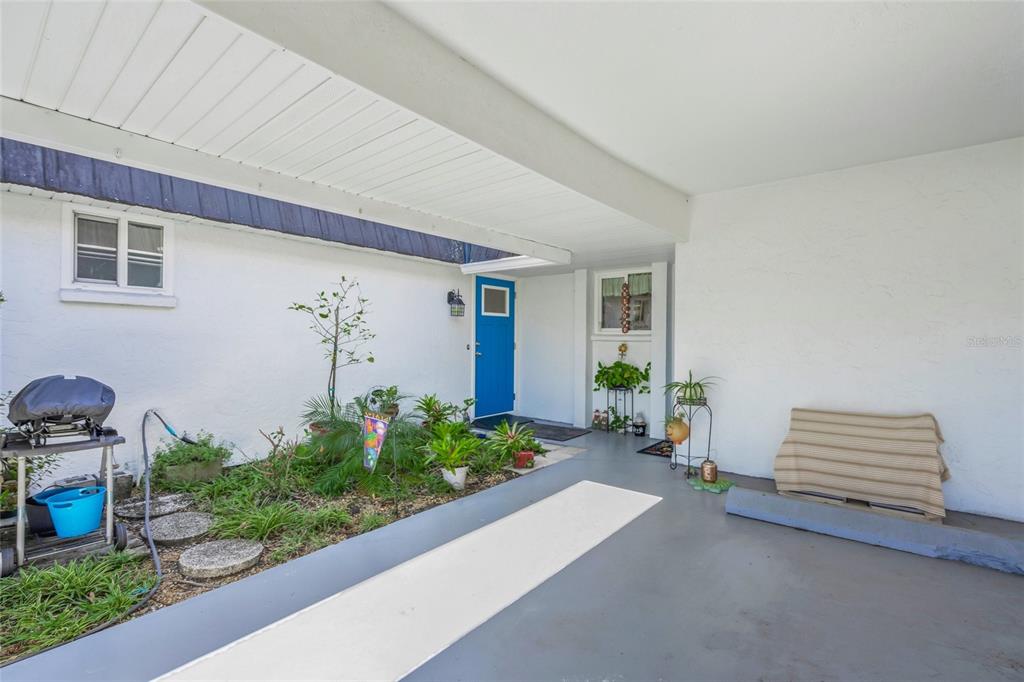 A covered entryway features a blue front door, a small garden bed, and concrete flooring — 1325 GLEN OAKS DRIVE E UNIT 133, SARASOTA, FL
