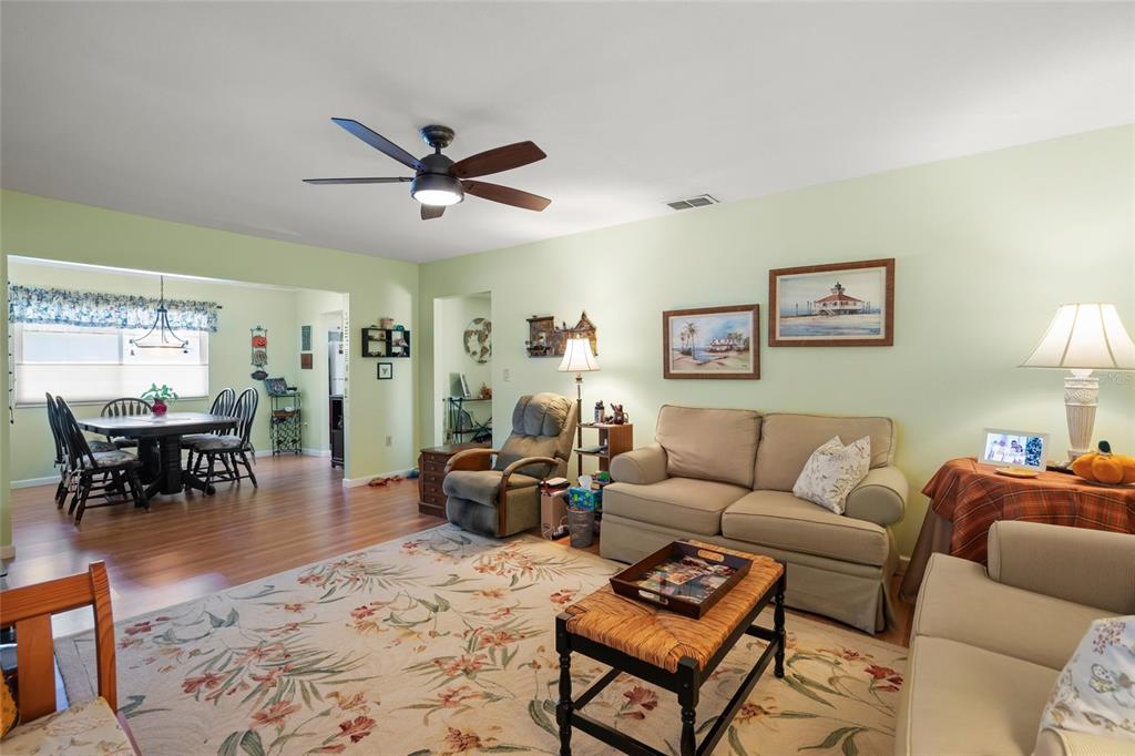 A living room with light green walls, a floral rug, and an adjacent dining area — 1325 GLEN OAKS DRIVE E UNIT 133, SARASOTA, FL