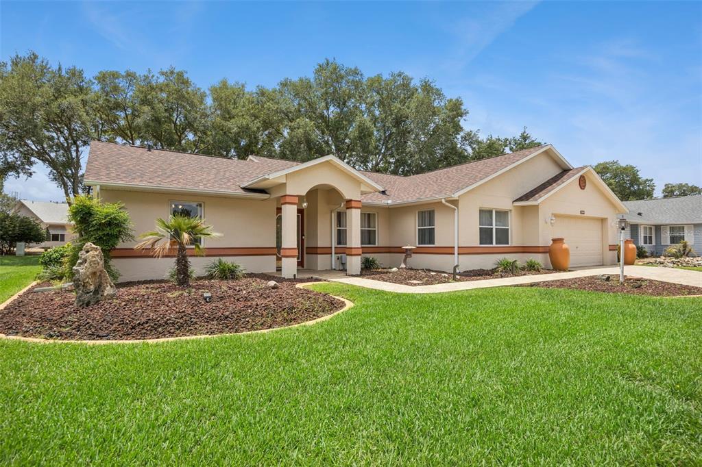 A single-story house with a tan stucco exterior, arched entryway, and a green lawn — 25904 NEWCOMBE CIRCLE, LEESBURG, FL