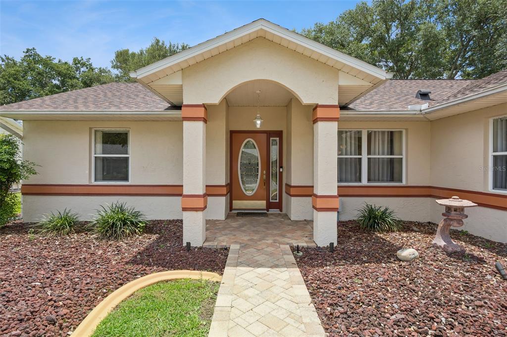 The exterior of a single-story house features a brick walkway leading to a covered entryway — 25904 NEWCOMBE CIRCLE, LEESBURG, FL