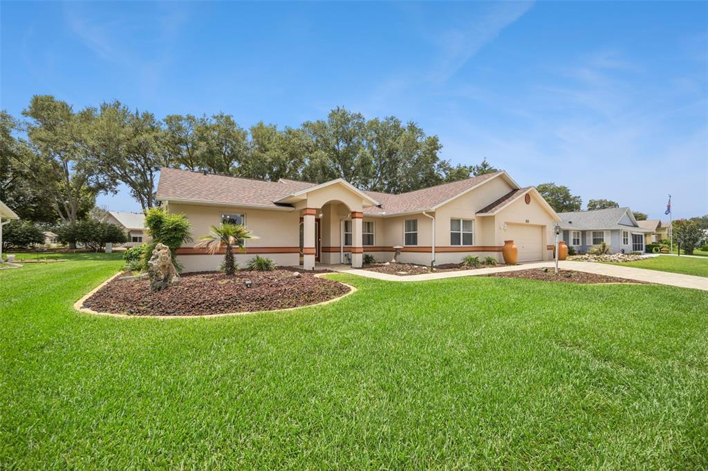 A single-story house with a tan exterior, a brown shingled roof, and a landscaped front yard — 25904 NEWCOMBE CIRCLE, LEESBURG, FL