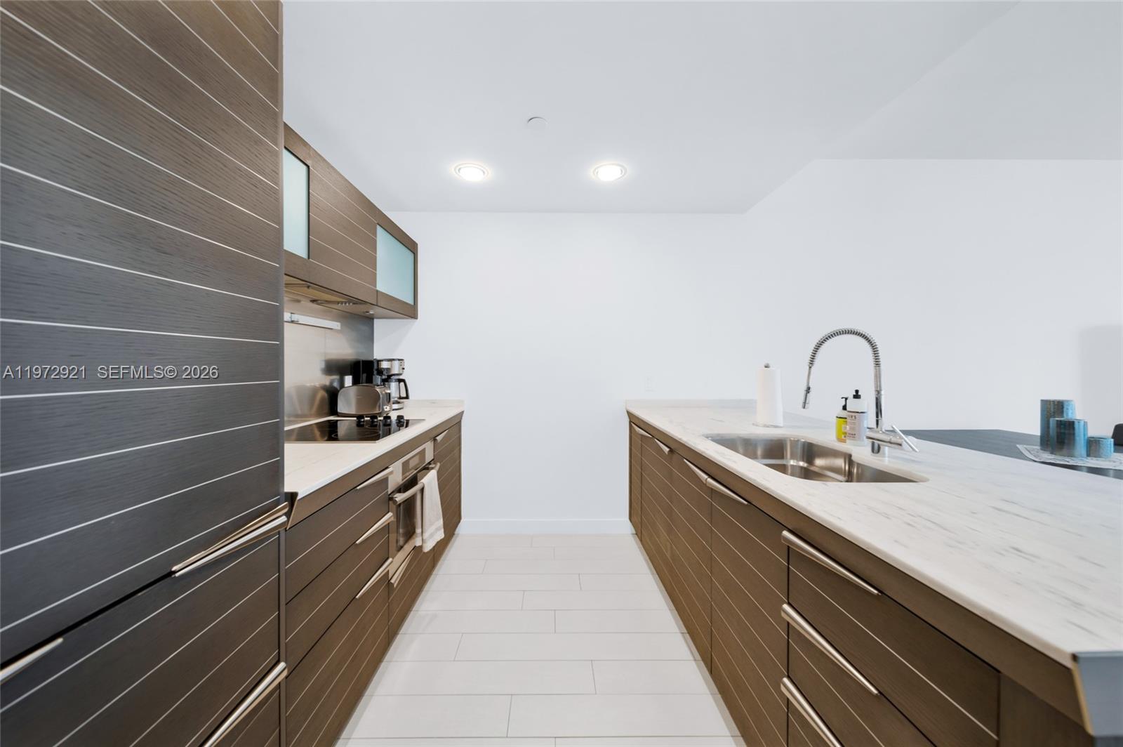 A modern galley kitchen features dark wood cabinetry, white countertops, and stainless steel appliances — 200 Biscayne Boulevard Way # 3811, Miami FL 33131, MIAMI, FL
