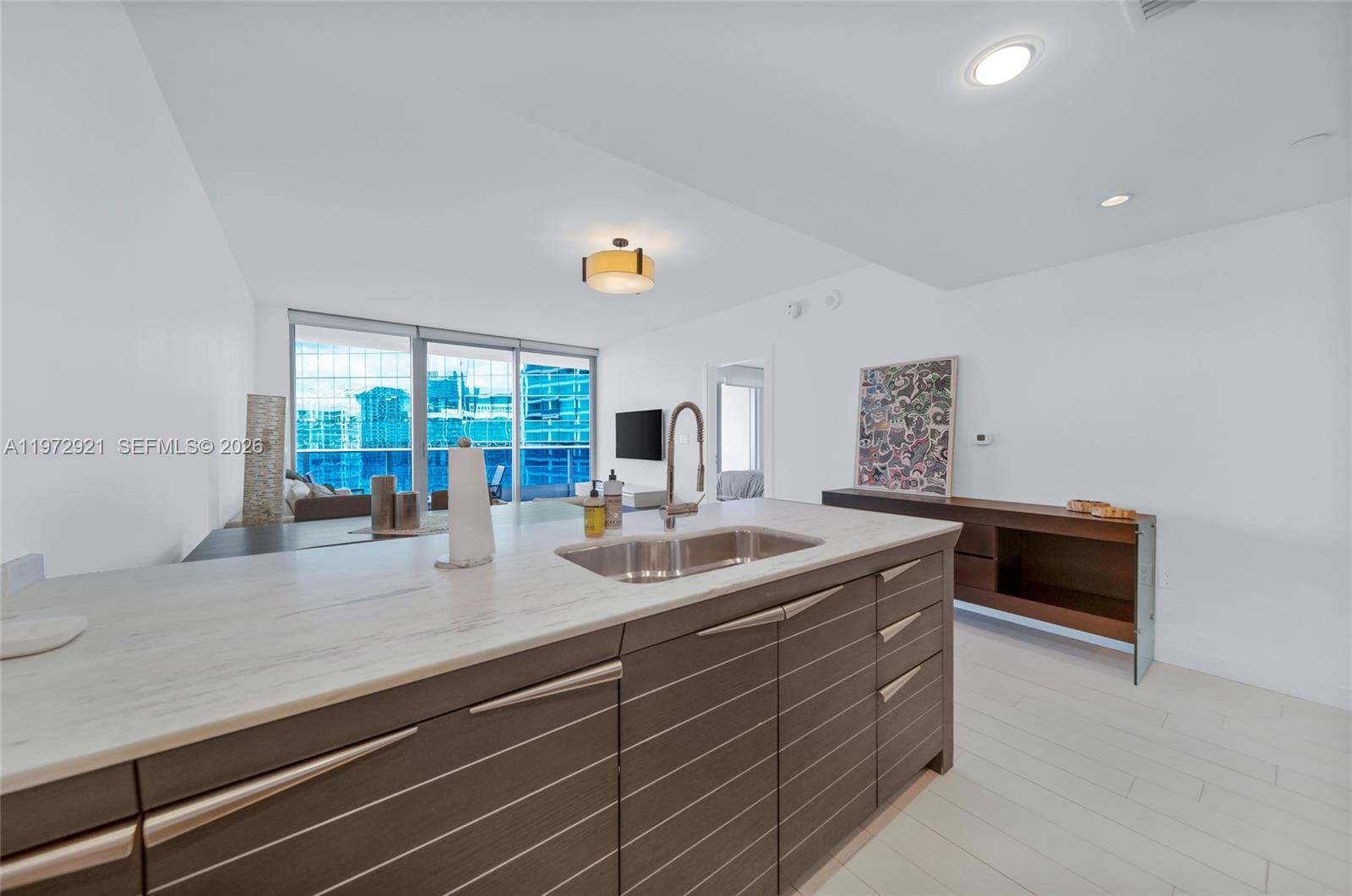 A kitchen island with a stainless steel sink sits in a modern, white-walled living space — 200 Biscayne Boulevard Way # 3811, Miami FL 33131, MIAMI, FL
