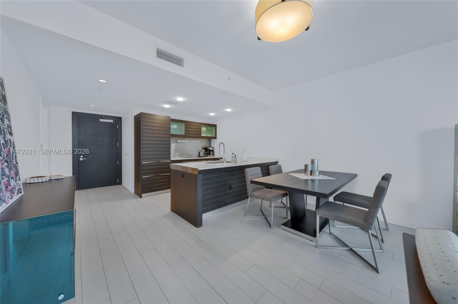 A modern kitchen features dark wood cabinetry, a central island, and an adjacent dining area — 200 Biscayne Boulevard Way # 3811, Miami FL 33131, MIAMI, FL