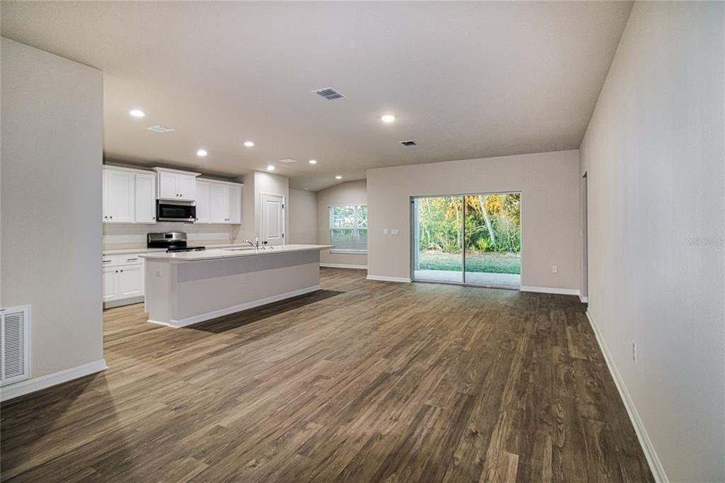 An open-concept kitchen with white cabinets and an island overlooks a living area with sliding doors — 2693 SW 155TH LANE, OCALA, FL