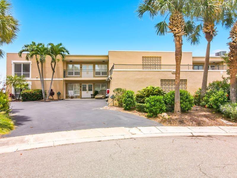 A two-story tan stucco building with palm trees and a paved parking area in front — 210 DOLPHIN POINT UNIT C, CLEARWATER BEACH, FL