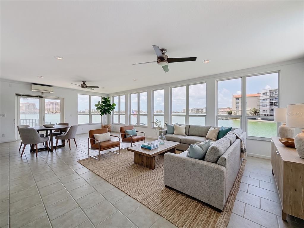A bright living and dining area features tile floors, neutral furniture, and large windows overlooking water — 210 DOLPHIN POINT UNIT C, CLEARWATER BEACH, FL