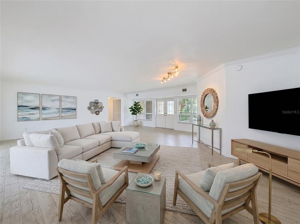 A bright living room features a large sectional sofa, two armchairs, and light wood flooring — 210 DOLPHIN POINT UNIT C, CLEARWATER BEACH, FL