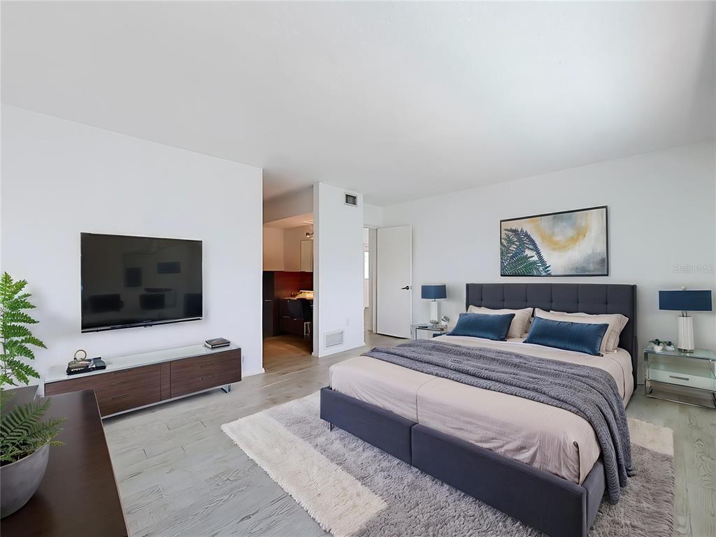A bedroom with a dark upholstered bed, a wall-mounted television, and light wood-look flooring — 210 DOLPHIN POINT UNIT C, CLEARWATER BEACH, FL