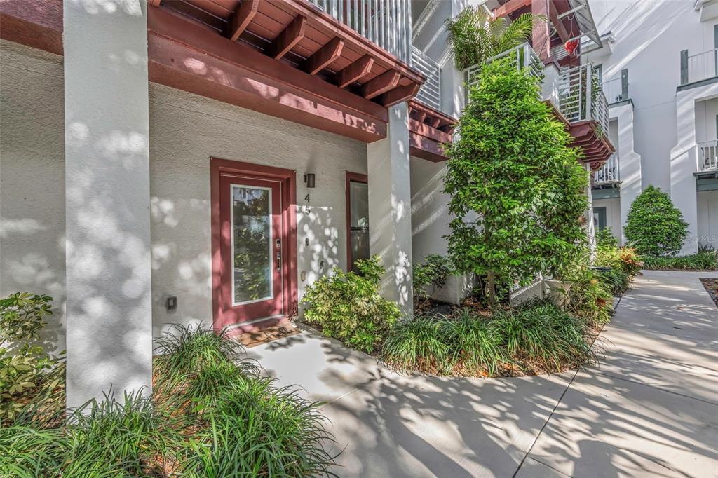 The exterior entrance of a multi-story residential building features a red door and landscaping — 946 HIGHLAND AVENUE UNIT 45, DUNEDIN, FL