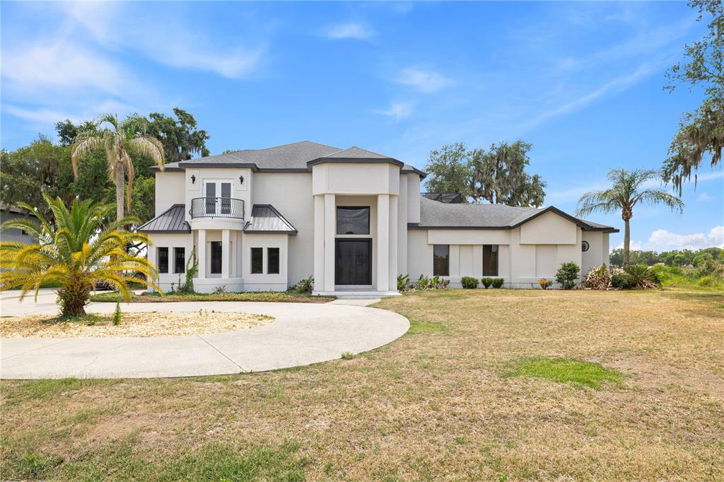 A two-story stucco house with a circular driveway, palm trees, and a dark metal roof — 10640 LAKE MINNEOLA SHORES, CLERMONT, FL