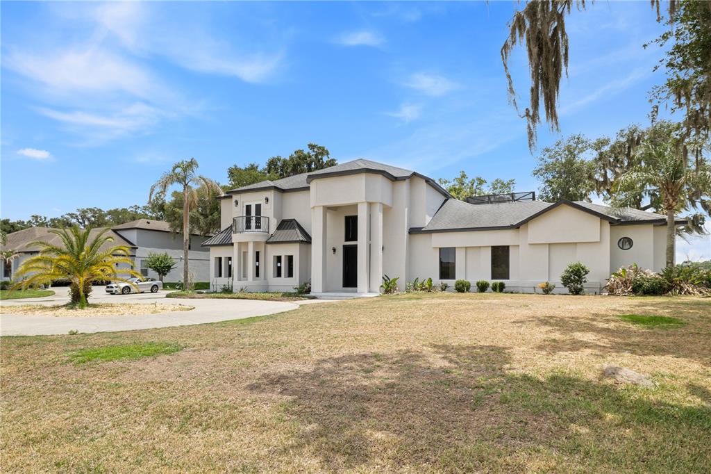 A two-story white stucco house features a prominent entryway, a balcony, and a circular driveway — 10640 LAKE MINNEOLA SHORES, CLERMONT, FL