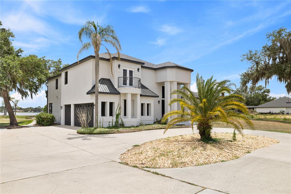 A two-story white house with a dark roof, balcony, and a large circular driveway — 10640 LAKE MINNEOLA SHORES, CLERMONT, FL