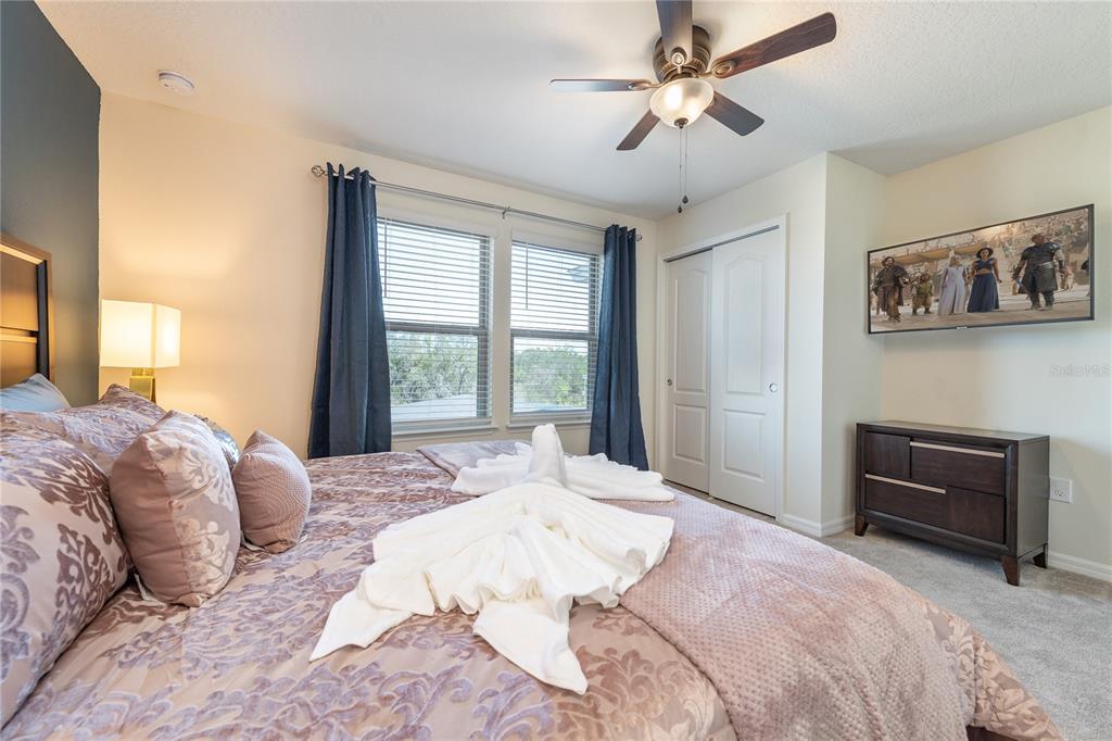 A bedroom features a bed with patterned bedding, a ceiling fan, and a wall-mounted television — 8931 ZURICH LANE, KISSIMMEE, FL
