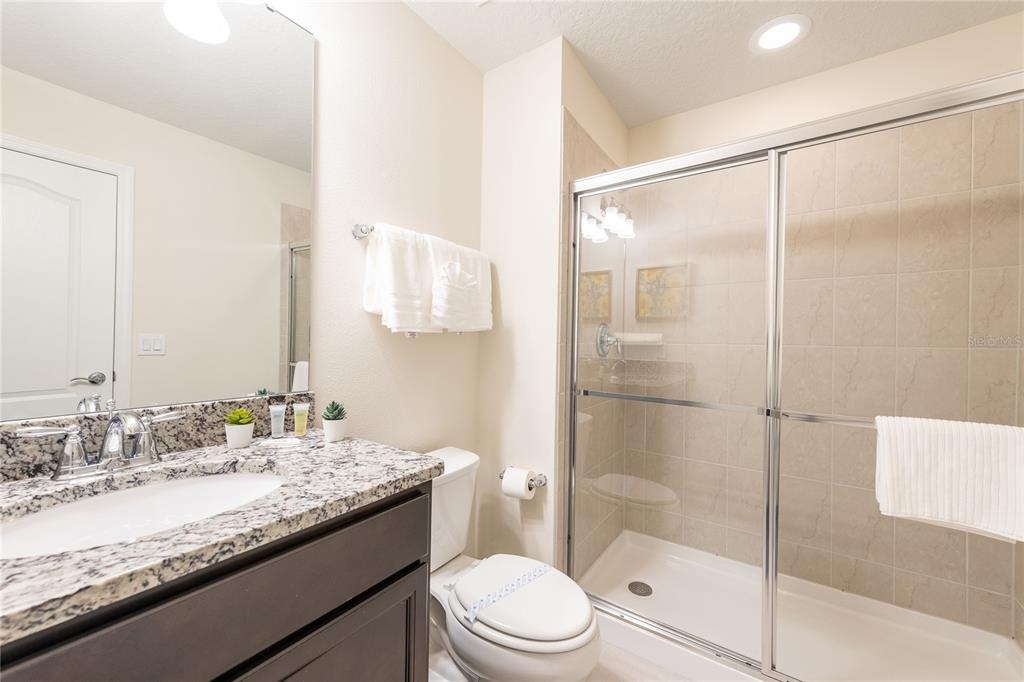 A bathroom features a granite vanity, a toilet, and a glass-enclosed walk-in shower — 8931 ZURICH LANE, KISSIMMEE, FL