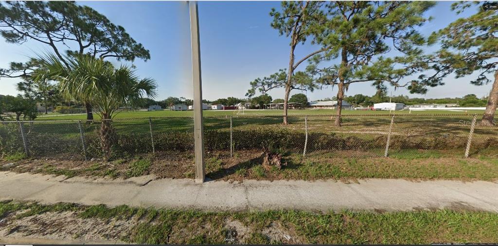 A chain-link fence borders a large, grassy vacant lot with several trees and a sidewalk — HWY 60 E, LAKE WALES, FL