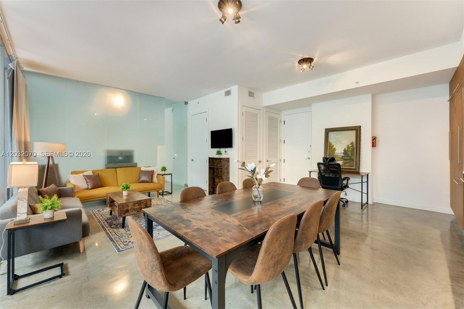 A living and dining area features a yellow sofa, wooden dining table, and concrete floors — 250 NW 24th St # 2B, Miami FL 33127, MIAMI, FL