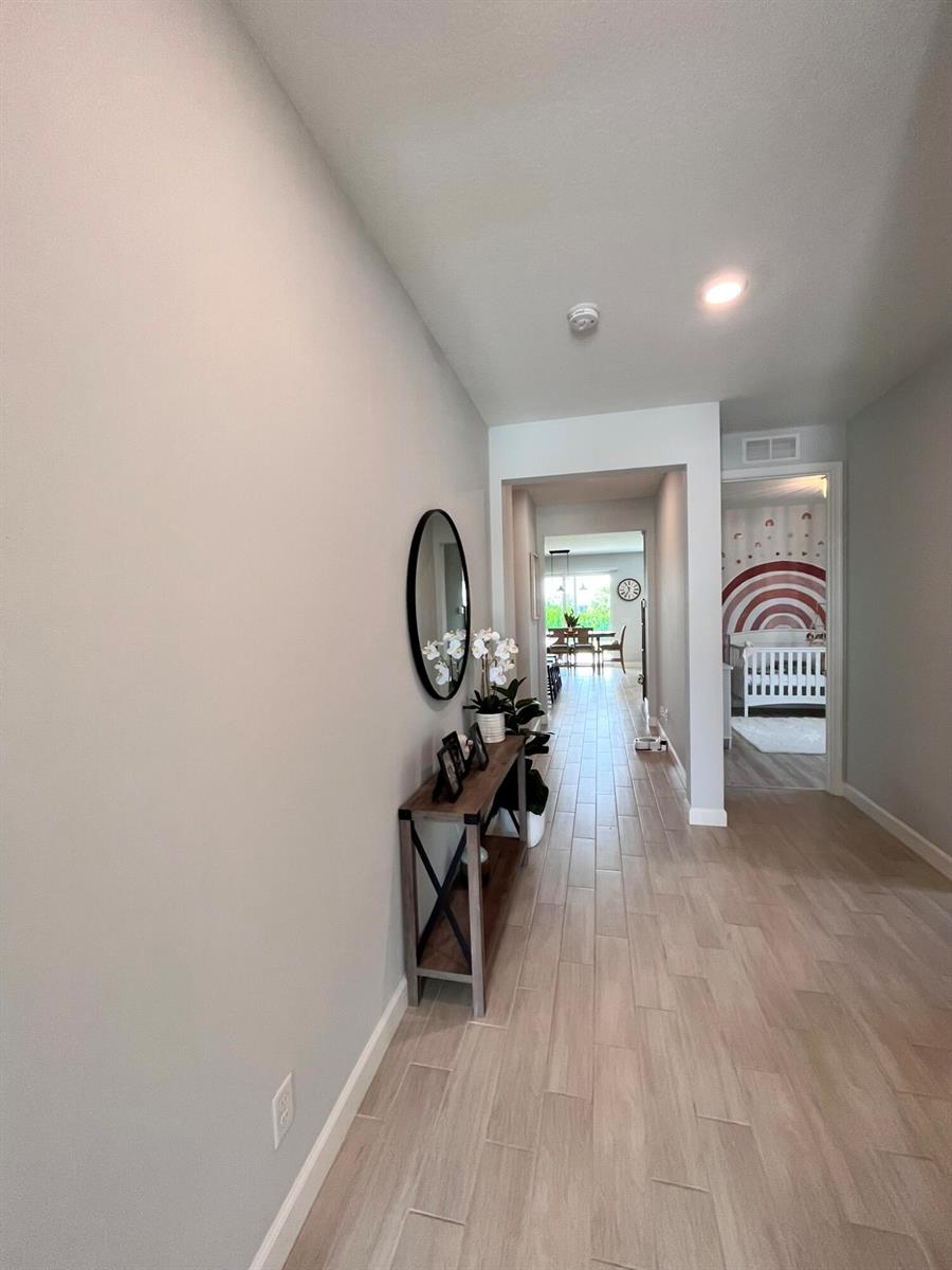 A hallway with light wood-look tile flooring leads to a dining area and a bedroom — 1272 Wandering Willow Way, Loxahatchee FL 33470, LOXAHATCHEE, FL
