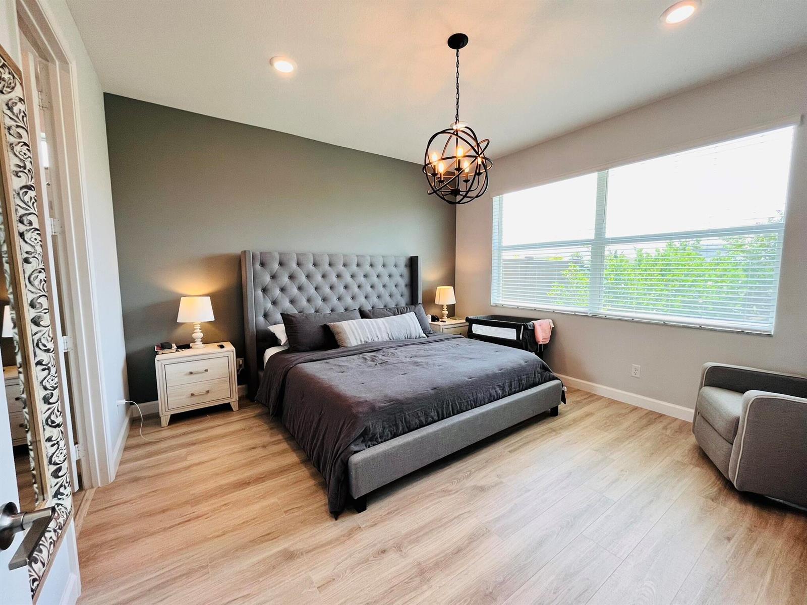 A bedroom features a tufted gray bed, a dark accent wall, and a globe chandelier — 1272 Wandering Willow Way, Loxahatchee FL 33470, LOXAHATCHEE, FL