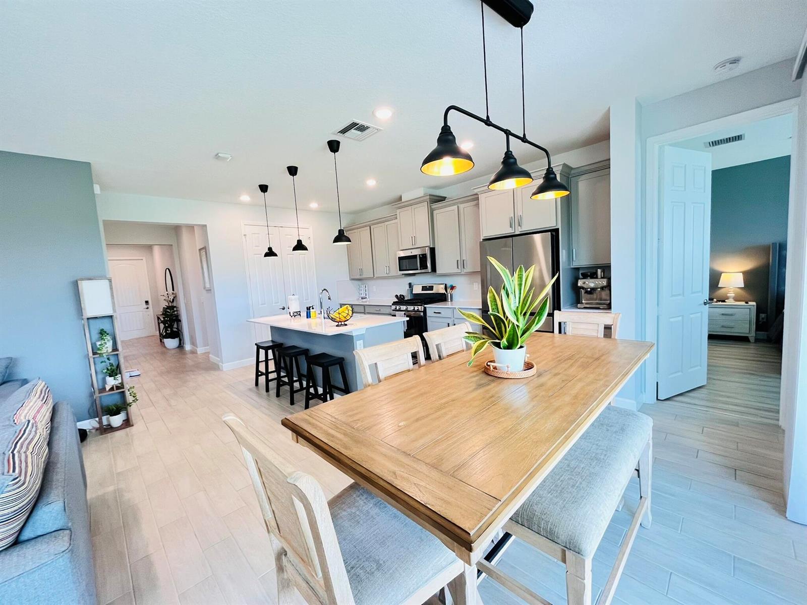 A dining area with a wooden table and bench sits before an open-concept kitchen — 1272 Wandering Willow Way, Loxahatchee FL 33470, LOXAHATCHEE, FL