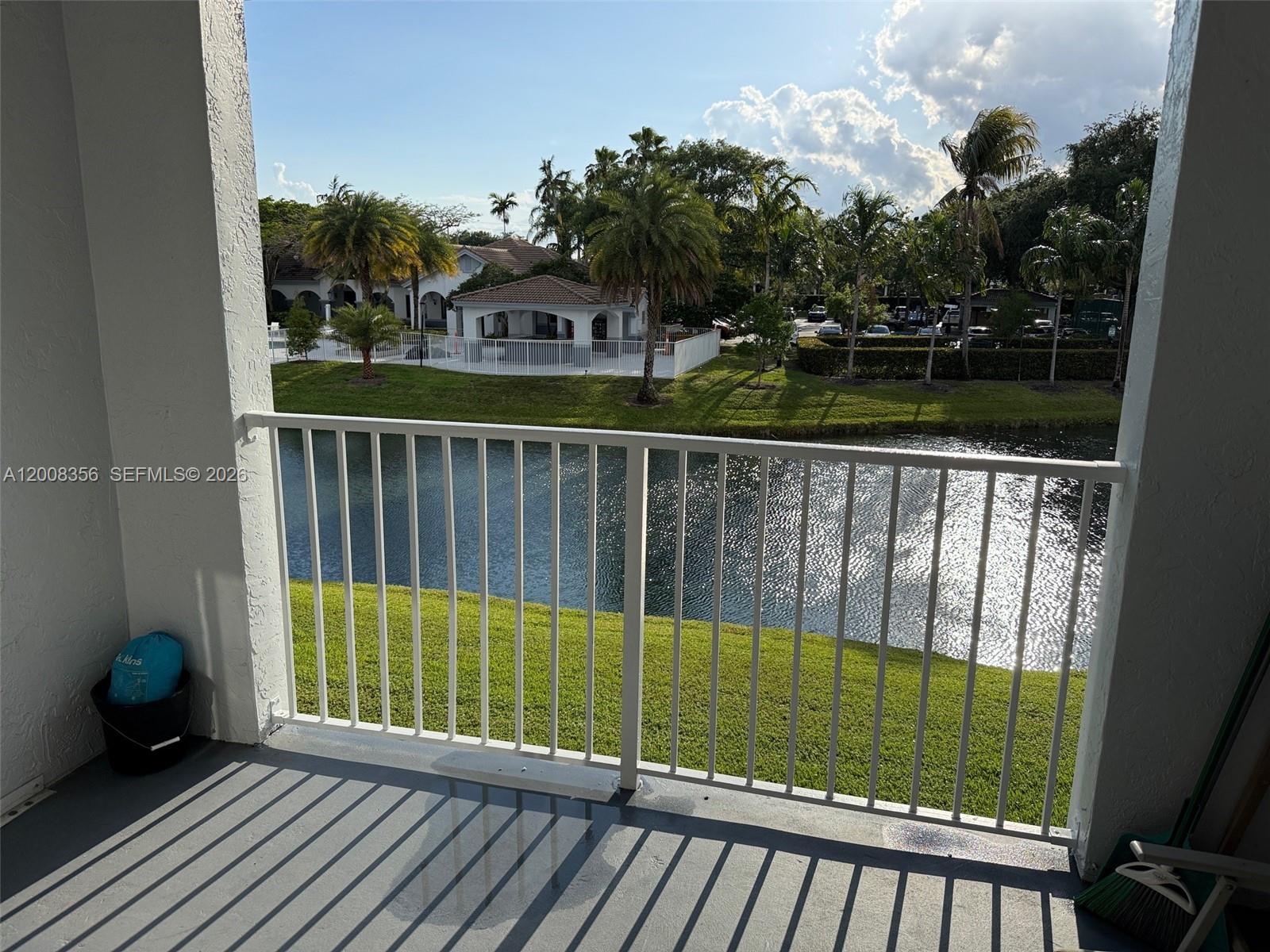 A balcony with a white railing overlooks a lake, green lawn, and palm trees — 2600 S University Dr # 226, Davie FL 33328, DAVIE, FL