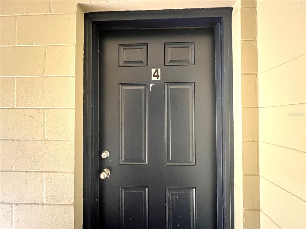 A dark-colored front door with the number four is set into a beige block wall — 1303 NW 6TH STREET UNIT 4, GAINESVILLE, FL