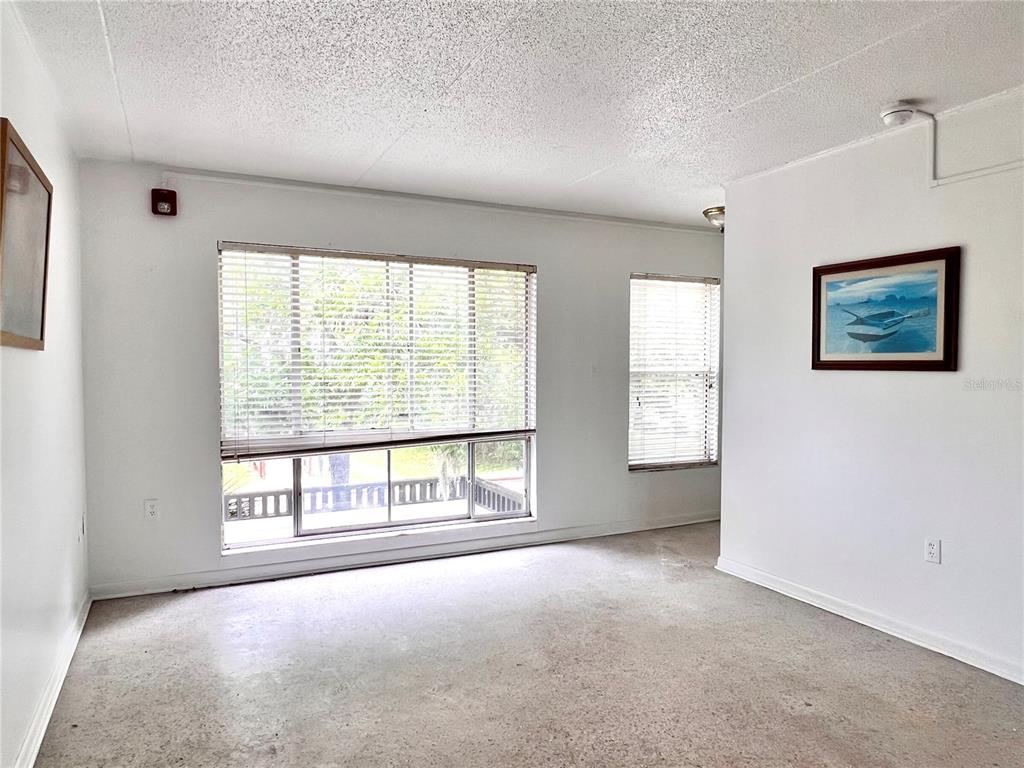 An empty room with beige carpet, white walls, two windows with blinds, and framed artwork — 1303 NW 6TH STREET UNIT 4, GAINESVILLE, FL