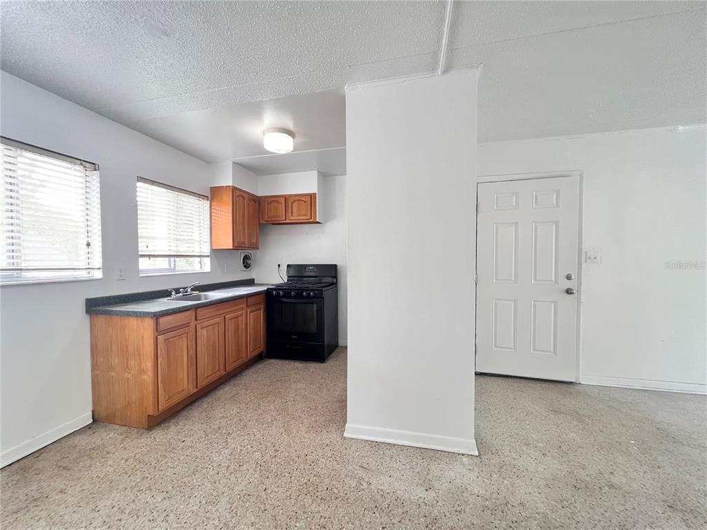 A kitchen with wooden cabinets, a black stove, and a sink, adjacent to a white door — 1303 NW 6TH STREET UNIT 4, GAINESVILLE, FL