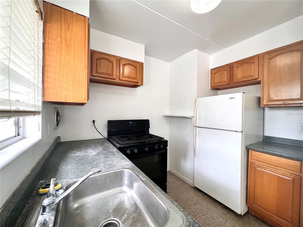A kitchen features wooden cabinets, a stainless steel sink, a black stove, and a refrigerator — 1303 NW 6TH STREET UNIT 4, GAINESVILLE, FL