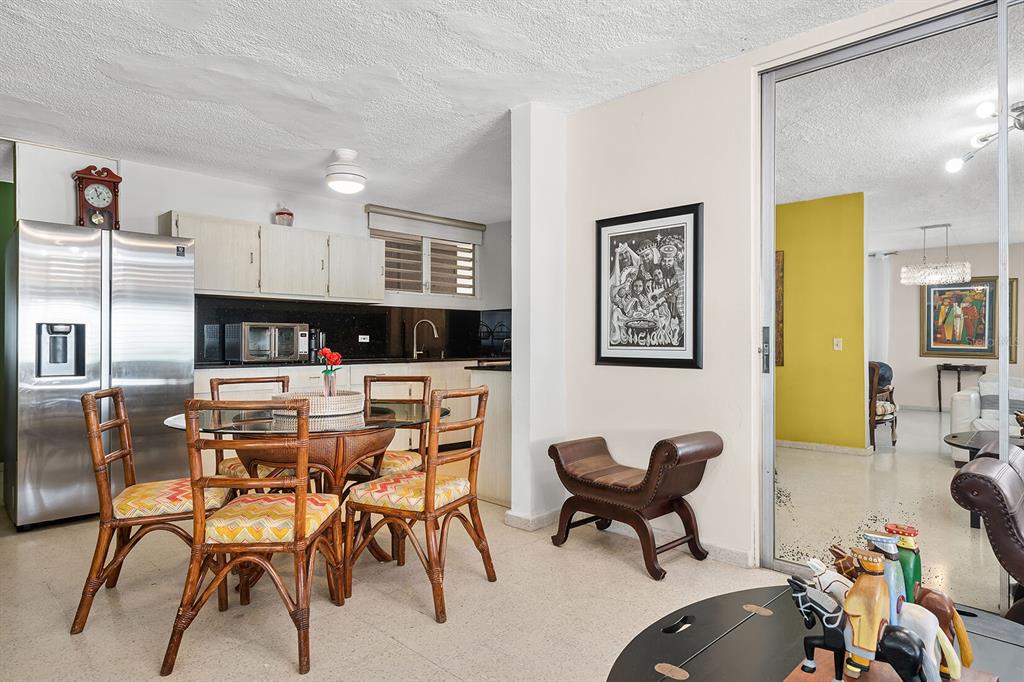 A dining area with a glass table and rattan chairs sits adjacent to a kitchen — Urb. Torrimar PASEO DE LA ALHAMBRA UNIT 1-16, GUAYNABO, PR