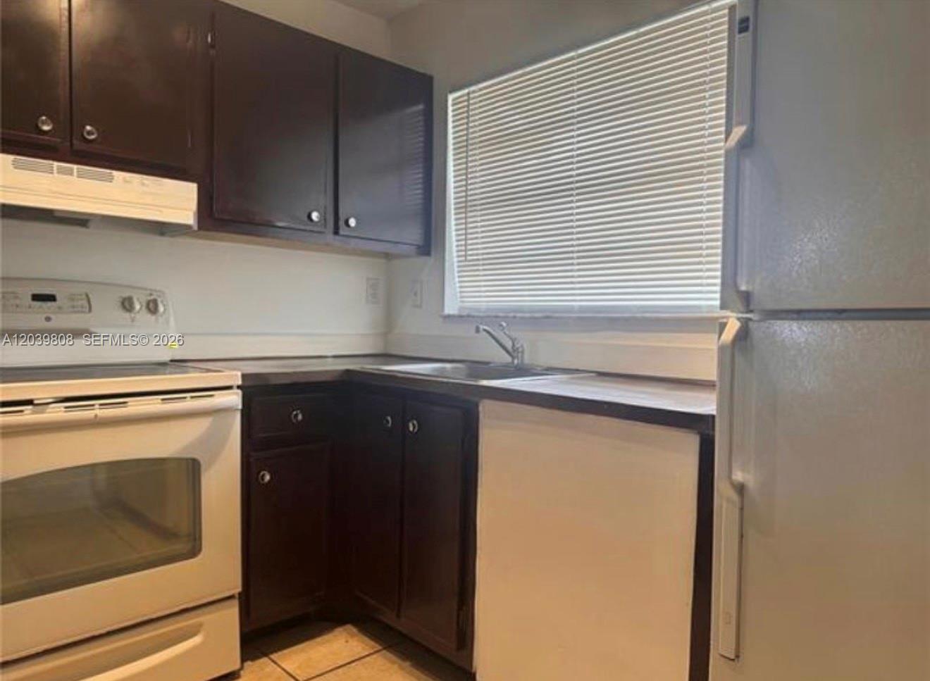 A kitchen features dark brown cabinets, white appliances, a window with blinds, and tile flooring — 819 NE 214th Ln # 1, Miami FL 33179, MIAMI, FL