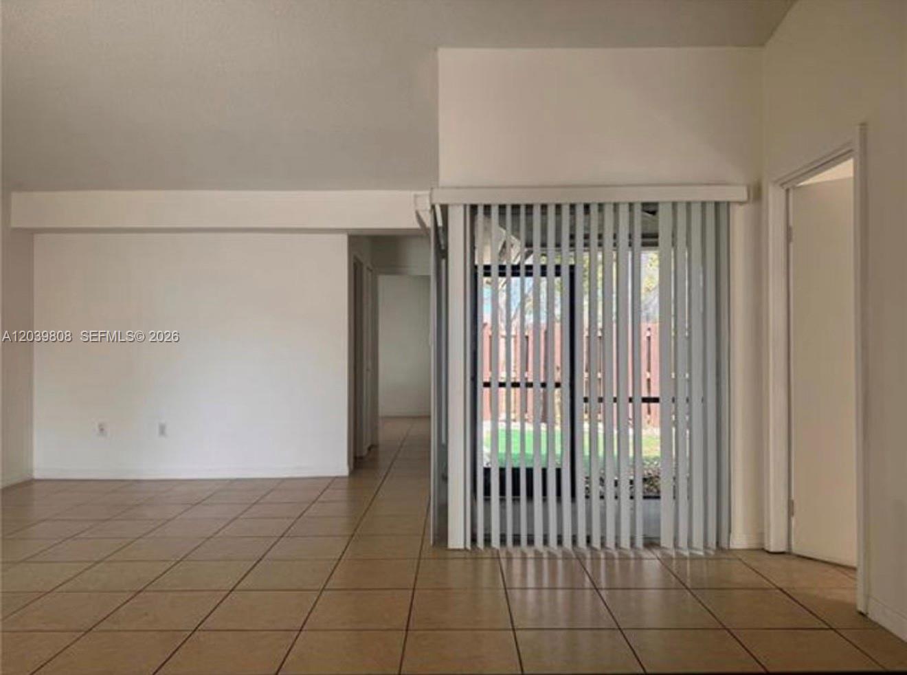 An interior room features light-colored tile flooring, white walls, and vertical blinds over a door — 819 NE 214th Ln # 1, Miami FL 33179, MIAMI, FL