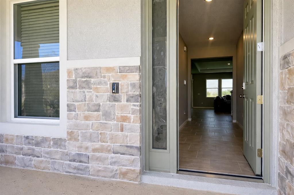 A view of a home entrance featuring a stone facade, window, and open front door — 33546 DARLEY DALE TRAIL, WESLEY CHAPEL, FL
