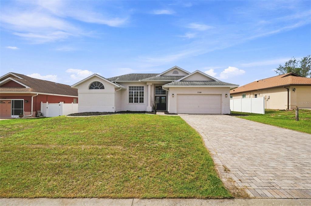 A single-story house with a beige stucco exterior, a two-car garage, and a paved driveway — 7258 ALOE DRIVE, SPRING HILL, FL