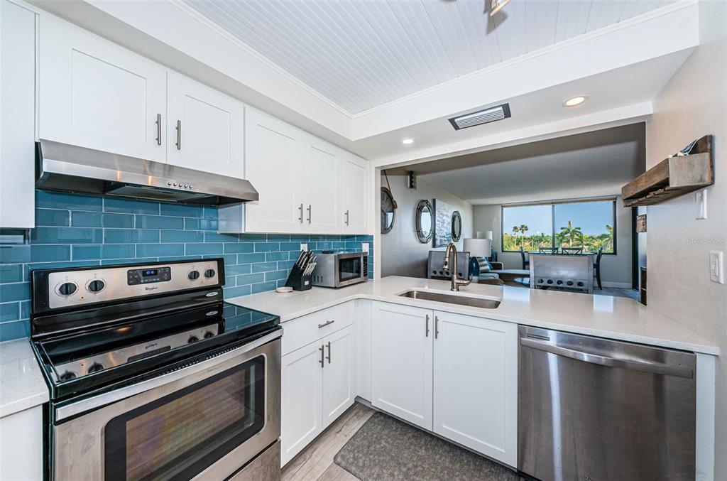 A kitchen features white cabinets, stainless steel appliances, a blue subway tile backsplash, and quartz countertops — 6361 BAHIA DEL MAR BOULEVARD UNIT 503, ST PETERSBURG, FL