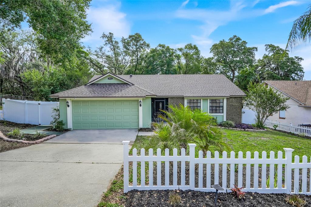 A single-story house with a green garage door and a white picket fence in front — 5933 GROVELINE DRIVE, ORLANDO, FL