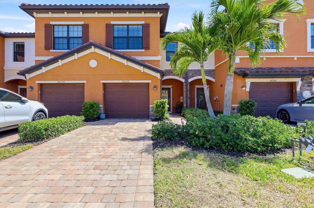 A multi-unit residential building with orange stucco walls, brown garage doors, and a paver driveway — 20352 LAGENTE CIRCLE, VENICE, FL
