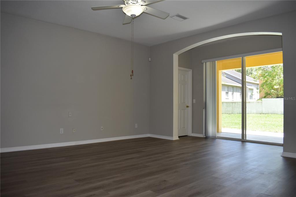 An empty living room features gray walls, wood-look flooring, a ceiling fan, and sliding glass doors — 644 CHESNEY DRIVE, VALRICO, FL