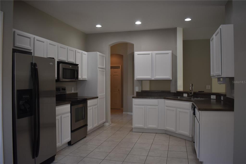 A kitchen features white cabinets, stainless steel appliances, dark countertops, and light tile flooring — 644 CHESNEY DRIVE, VALRICO, FL