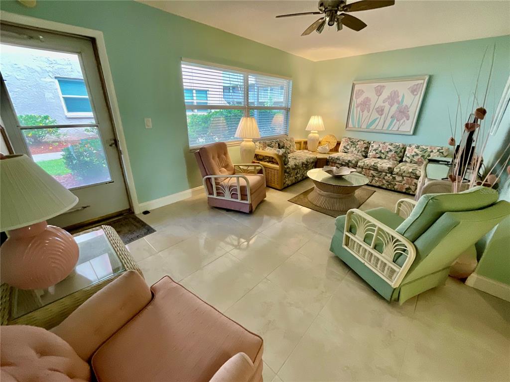 A sunlit living room features light green walls, tile flooring, and floral-patterned furniture — 10034 64TH AVENUE N UNIT 11, ST PETERSBURG, FL